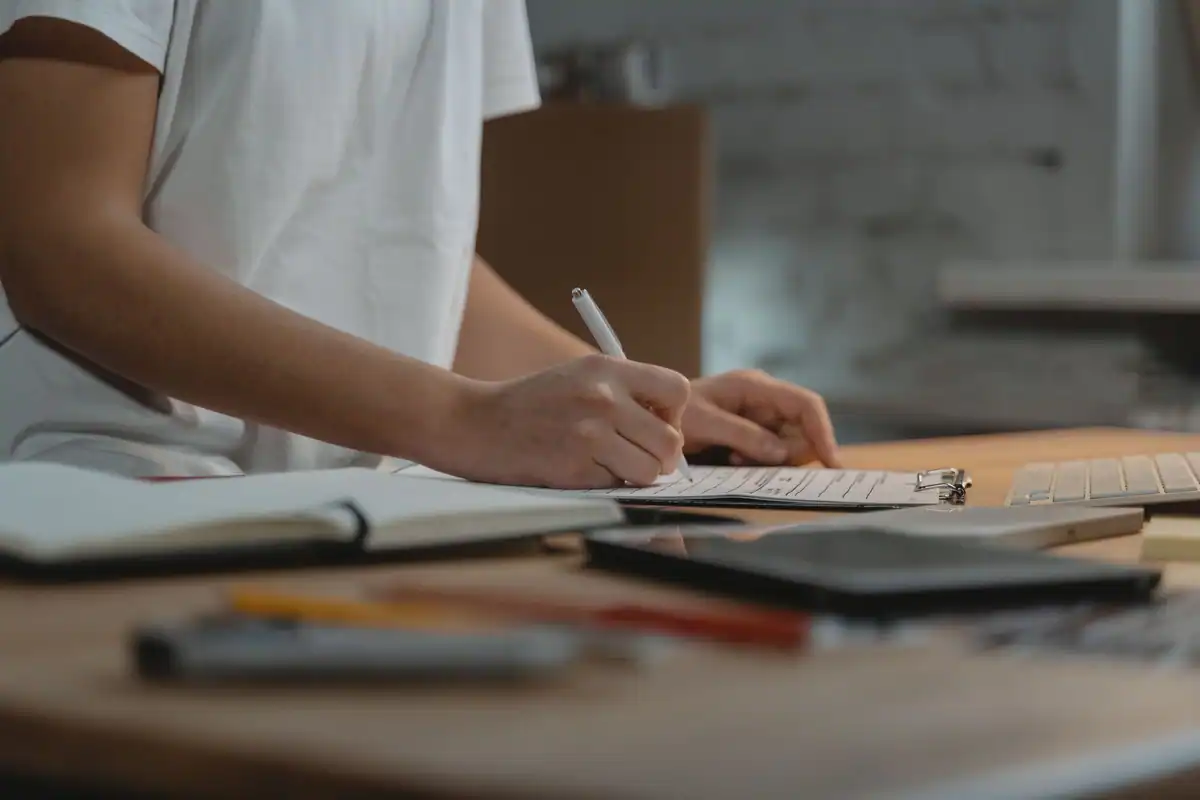 Mână care notează cerințele proiectului pe un clipboard, pe un birou cu papetărie