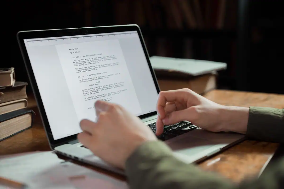 Persoană care redactează un document pe laptop, într-un colț de lucru cu cărți