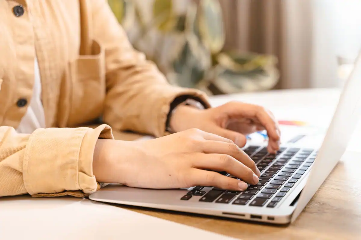 Mâini care tastează pe laptop într-un spațiu luminos de lucru