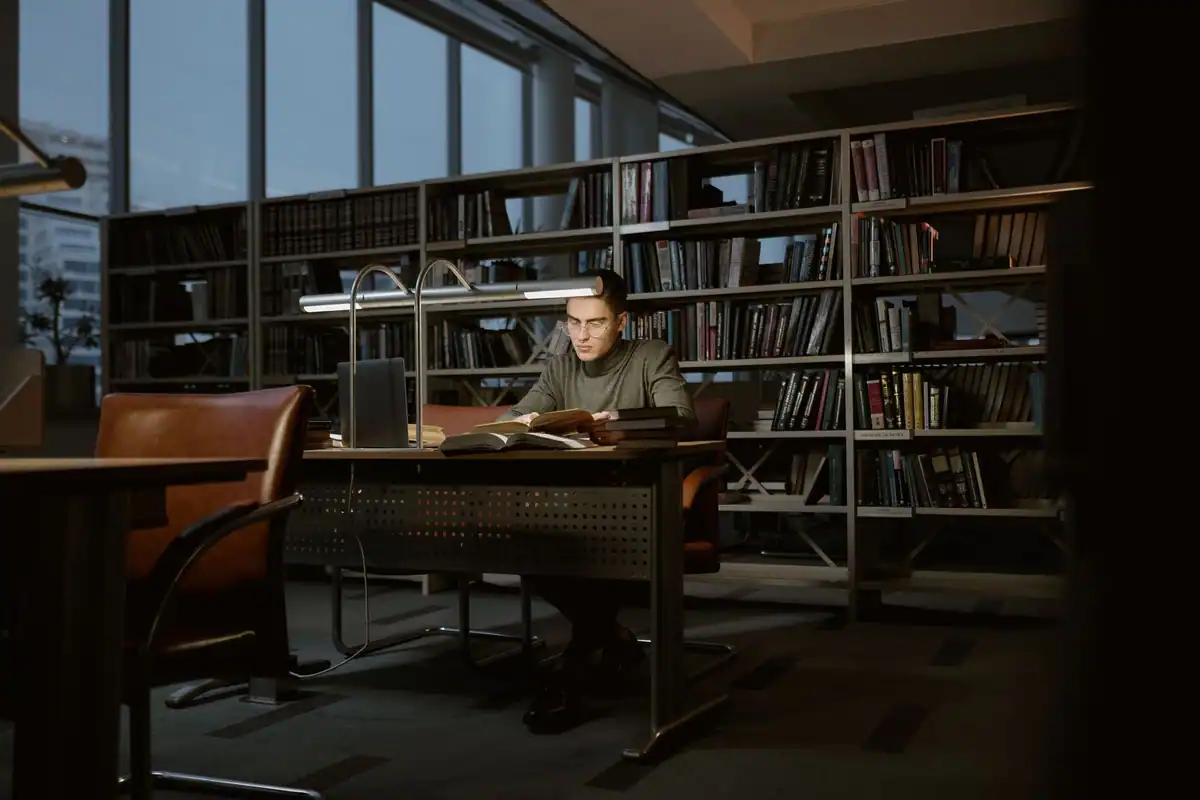 Tânăr care învață concentrat într-o bibliotecă liniștită, înconjurat de cărți