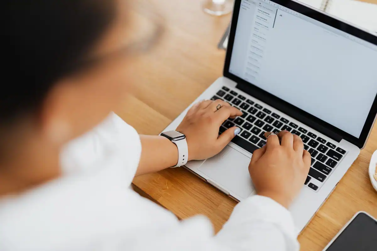 Persoană care tastează un mesaj pe laptop, văzută de sus, cu accent pe mâini
