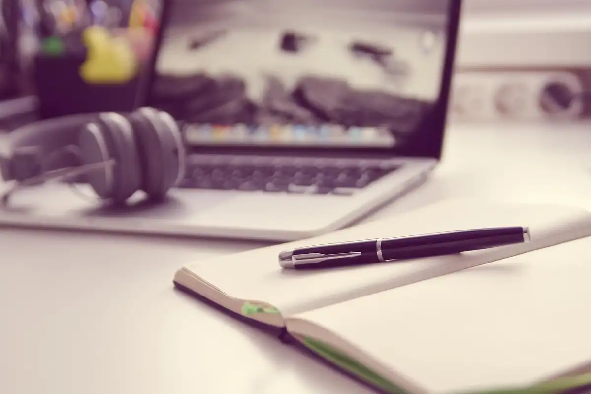Laptop, căști și caiet pe un birou de studiu, imagine despre învățarea limbii engleze pe lângă program