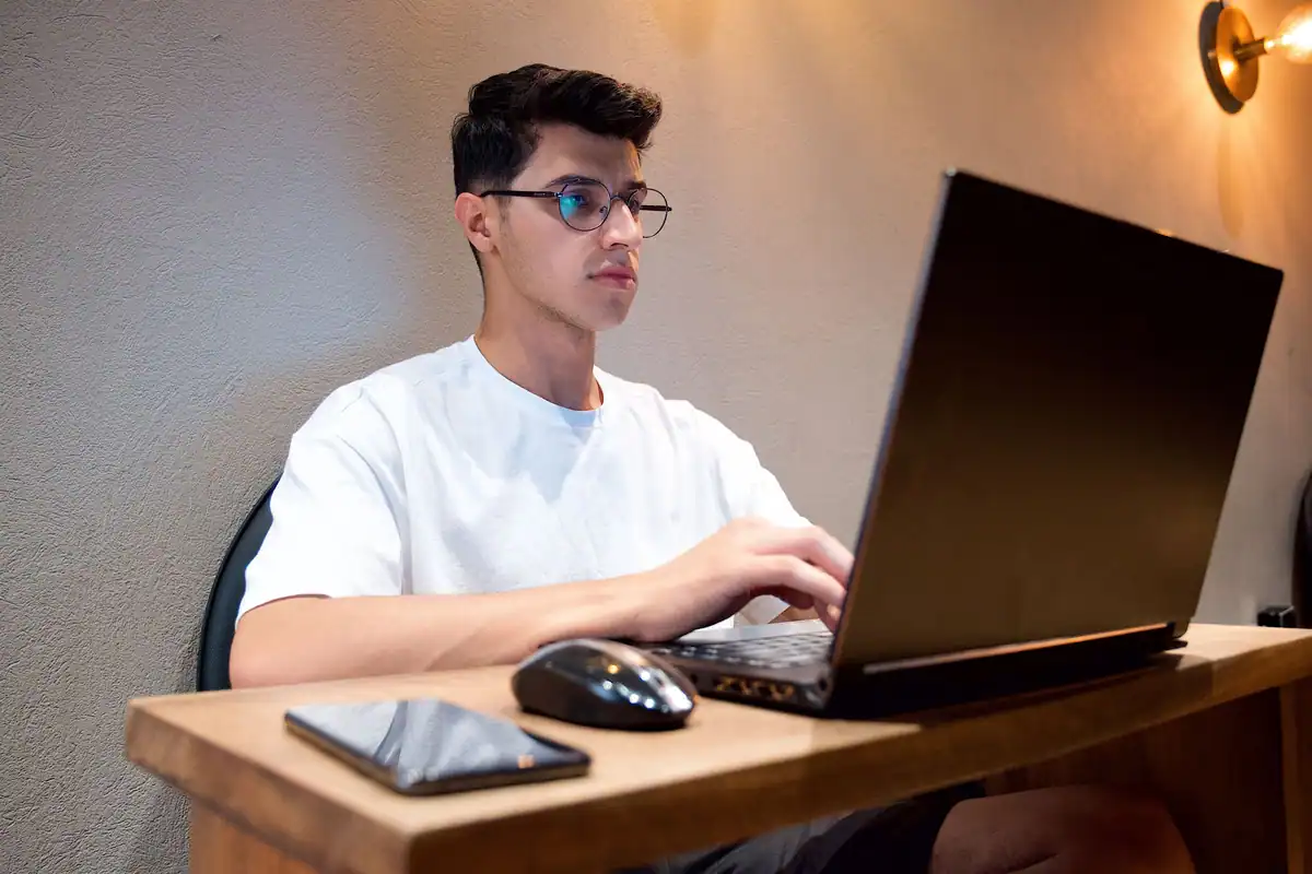 Bărbat în cămașă albă care lucrează pe laptop, cu telefonul și mouse-ul lângă el