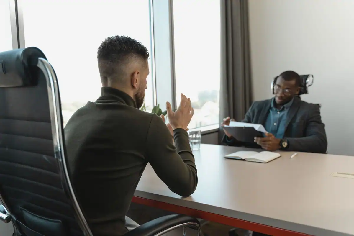 Doi bărbați la un interviu de angajare, într-un birou cu ferestre mari