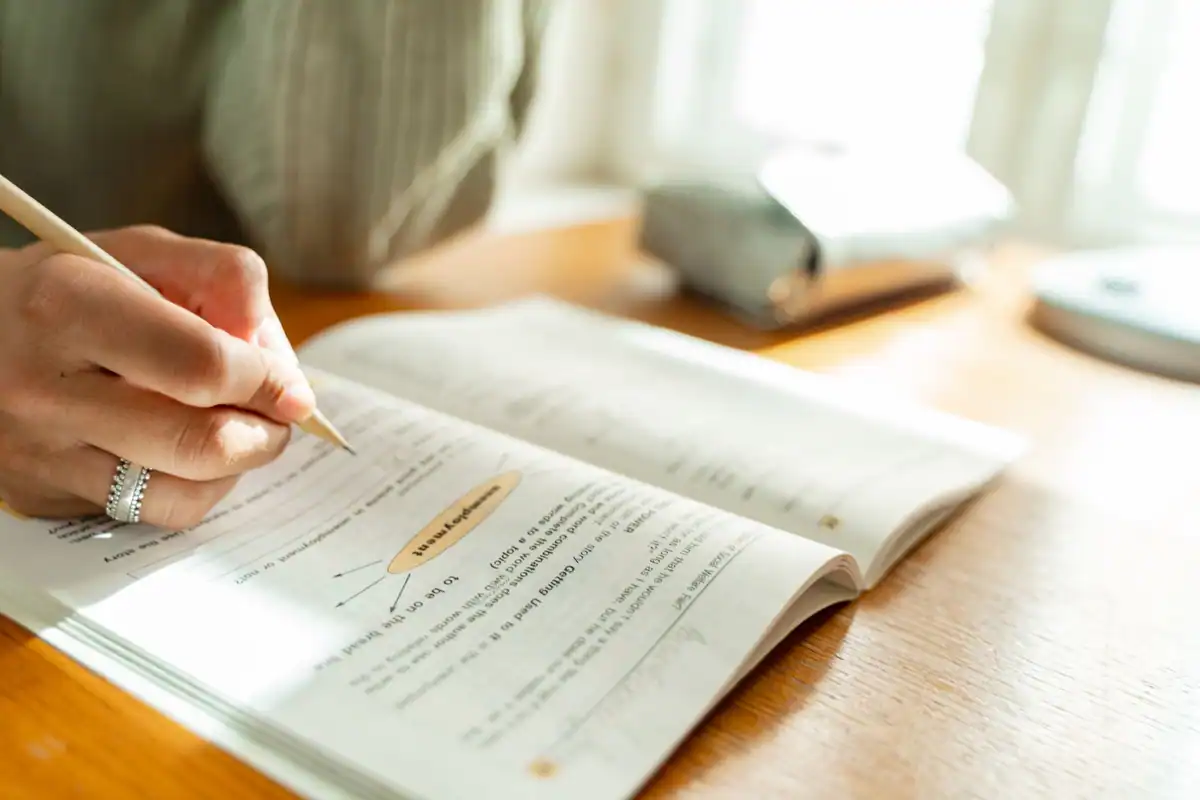 Student care ia notițe într-un manual, la un birou însorit