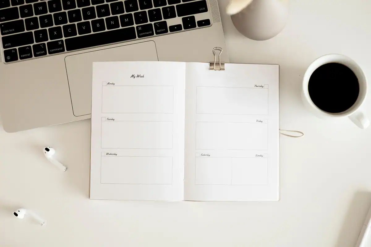 Birou văzut de sus, cu planner, cafea, laptop și căști, într-un stil minimalist