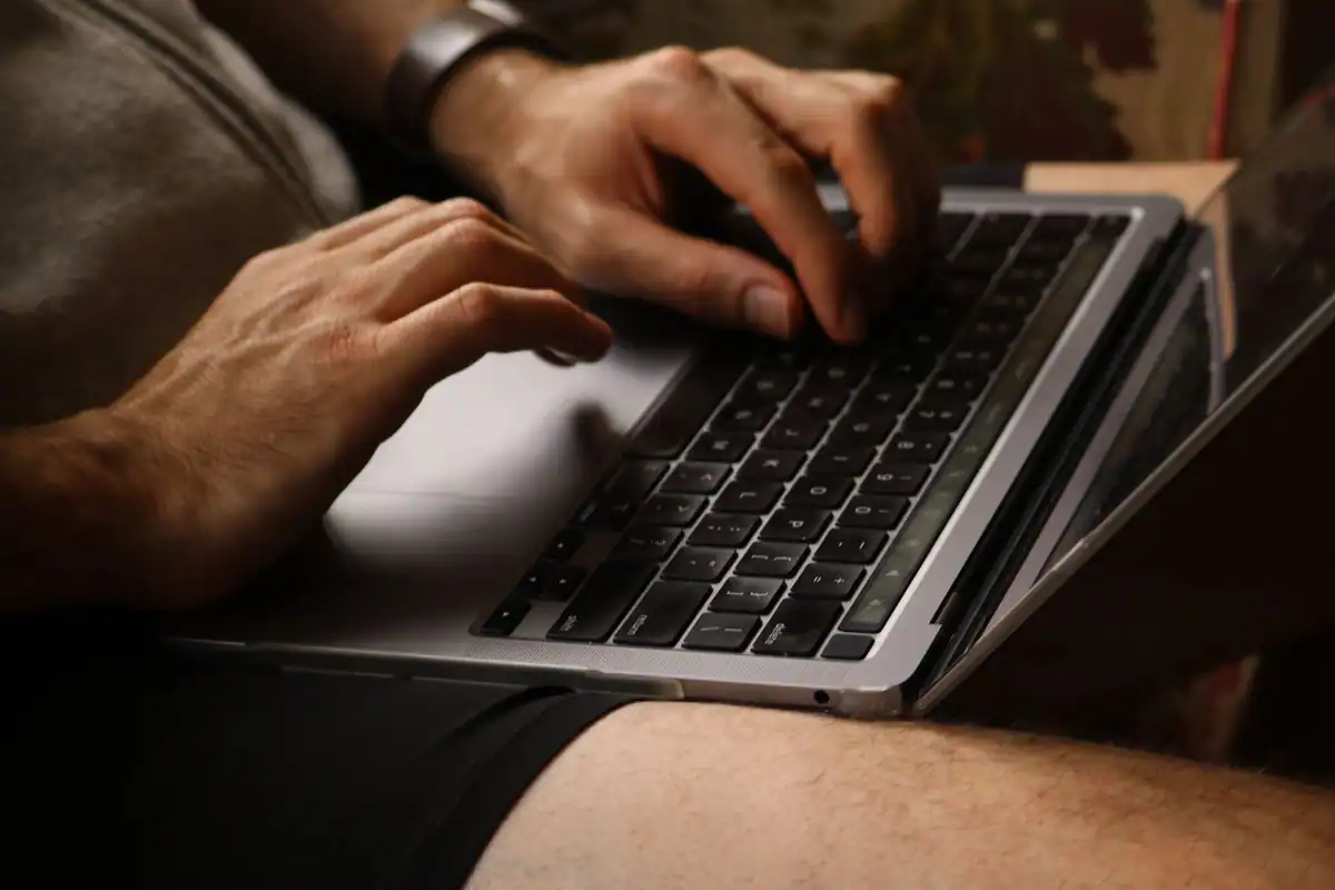Mâini care tastează pe laptop, în prim-plan, într-un spațiu de lucru obișnuit
