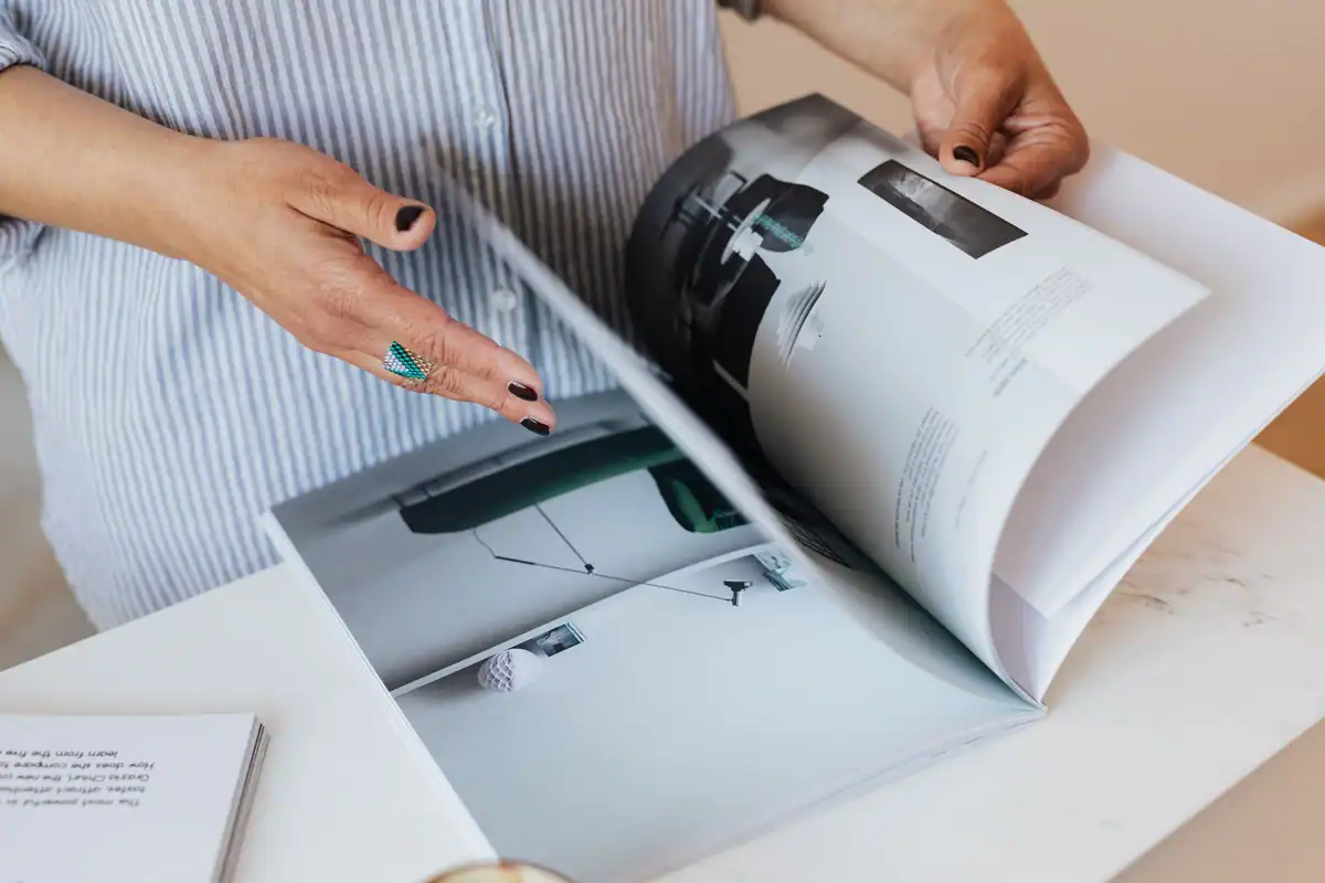 Mâini care răsfoiesc o revistă de design lângă o masă albă din marmură
