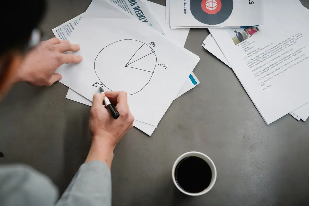 Bărbat care desenează o diagramă circulară pe hârtie, lângă o cafea