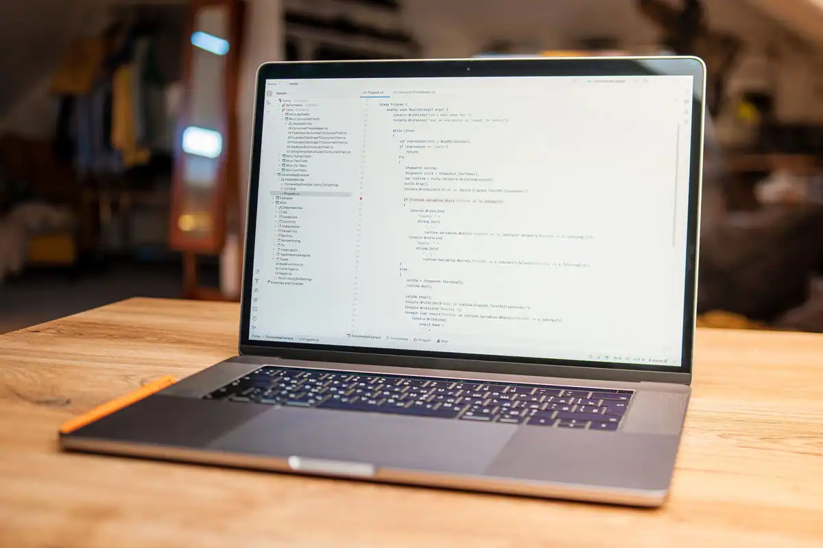 Laptop deschis cu cod pe ecran, pe un birou din lemn, într-un colț de lucru primitor