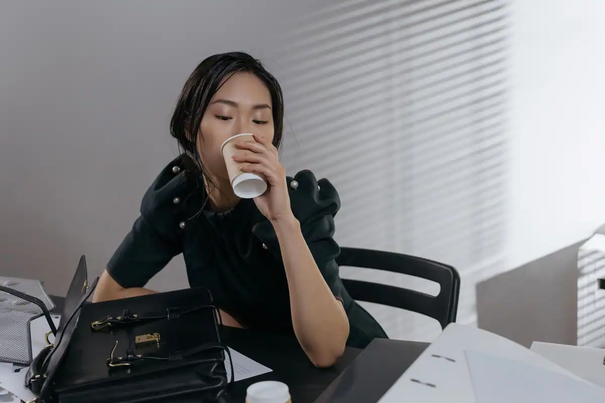 Femeie în bluză neagră care bea o cafea la un birou de lucru