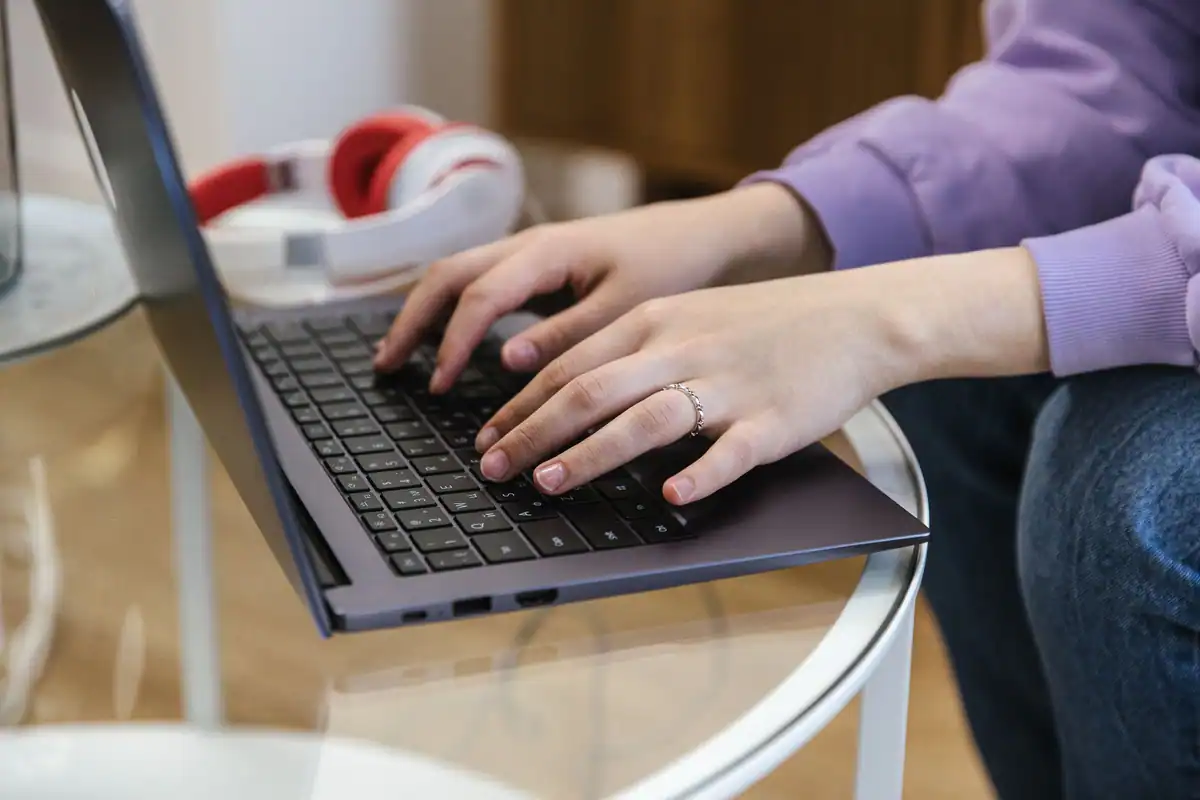 Mâini care tastează pe laptop, într-un spațiu interior cu căști roșii alături