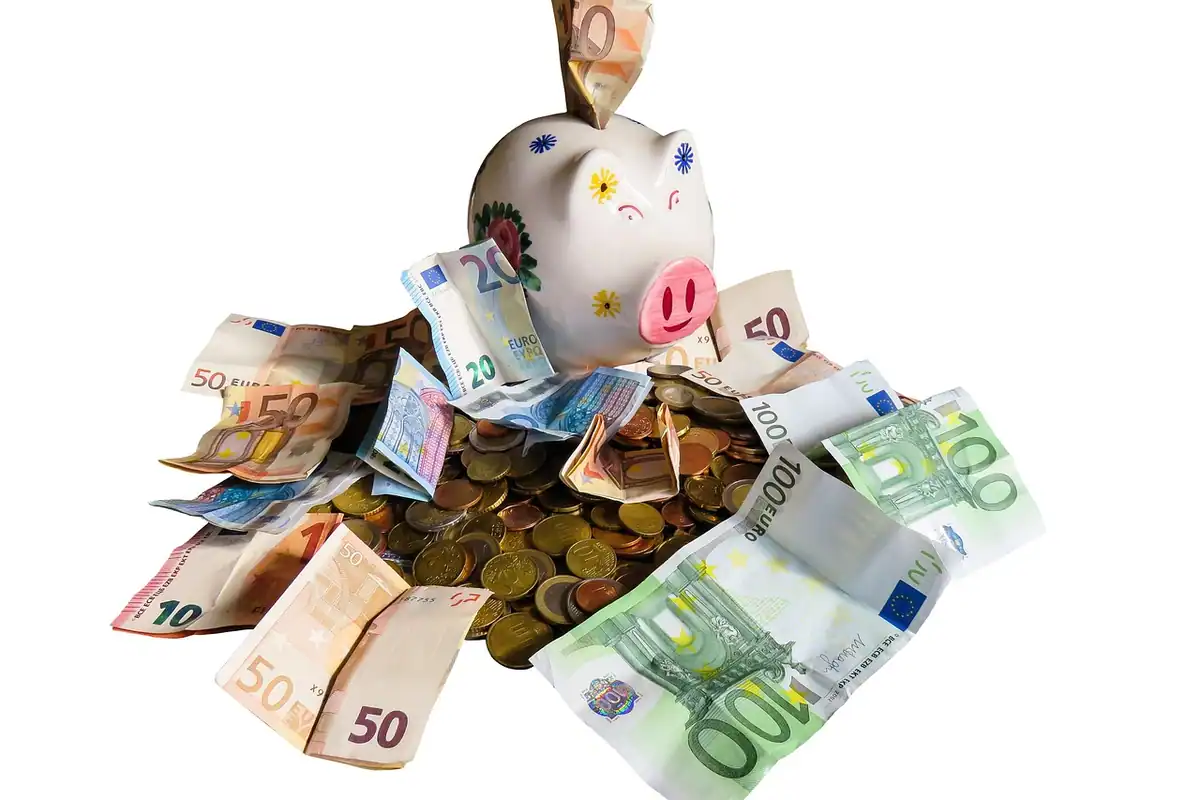 Pușculiță cu monede și caiet pe masă, imagine despre fondul de rezervă pentru venituri neregulate